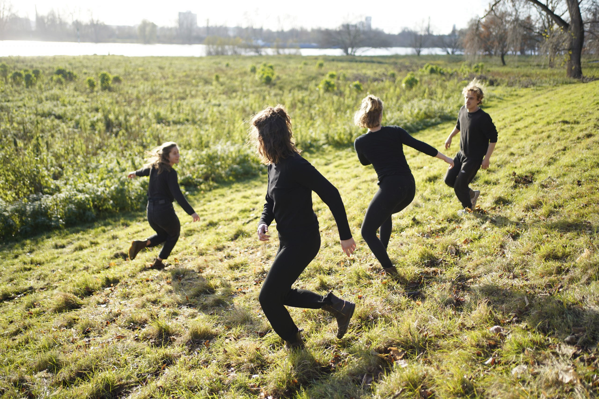 Vier Personen in schwarzen Kleidern spielen und rennen auf einem grasbewachsenen Hügel.