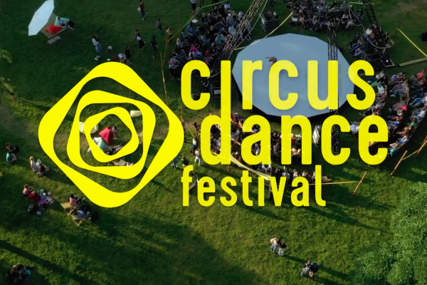 Luftaufnahme eines Freiluft-Zirkus-Tanzfestivals mit gelbem Logo in der Mitte der Wiese.