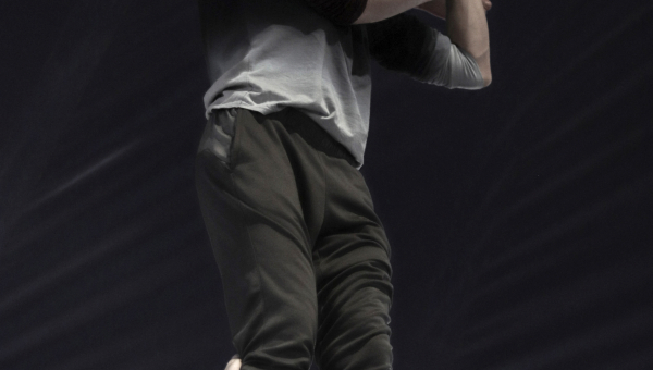 Drei Personen führen eine akrobatische Pyramide vor, wobei einer auf den Schultern eines anderen steht und den dritten trägt.