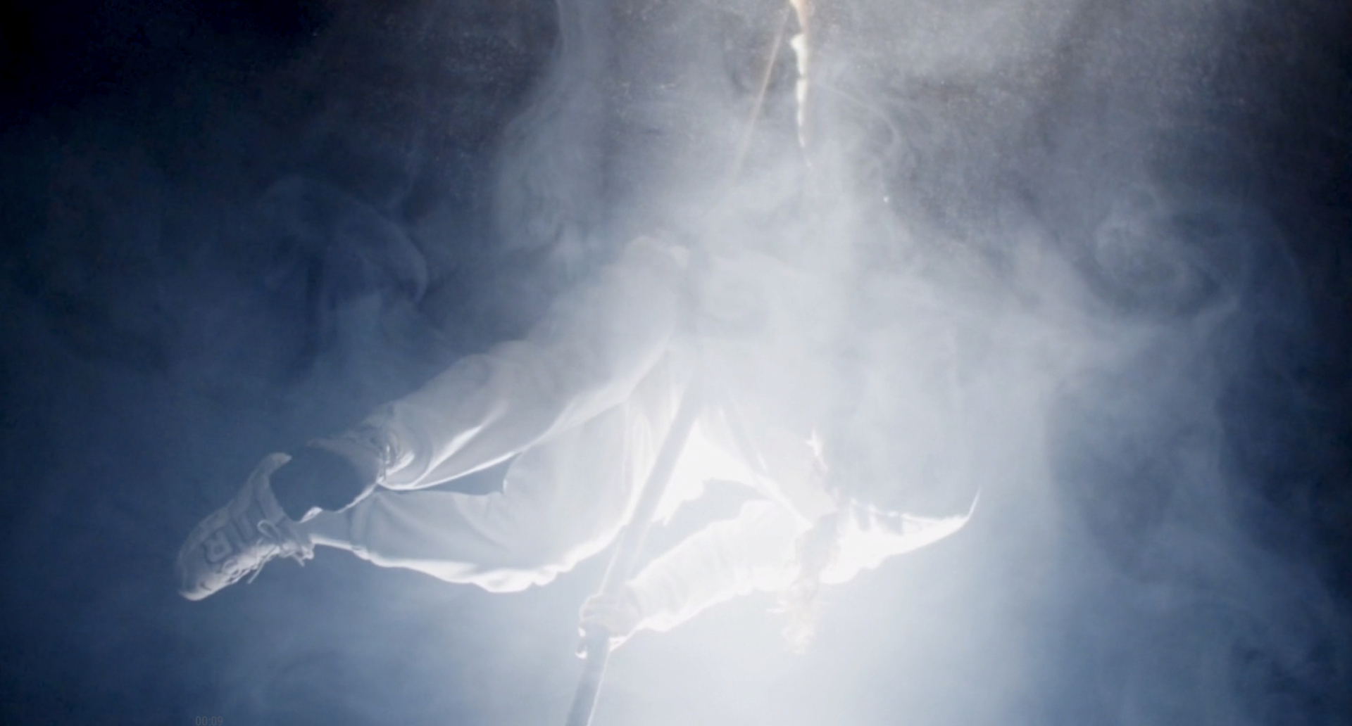 Eine Person in weißer Kleidung schwebt in einem dichten Nebel mit einem Lichtschein im Hintergrund.