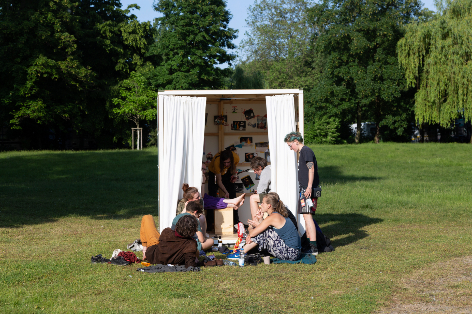 A group of people sits on the grass in front of a white, open booth decorated with